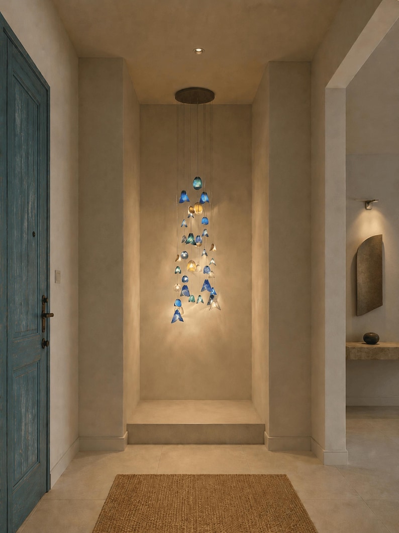 May include: A multi-pendant chandelier featuring numerous small, bell-shaped glass shades in varying shades of blue, teal, and clear glass. The pendants are suspended at different heights from a circular ceiling mount, creating a cascading effect.
