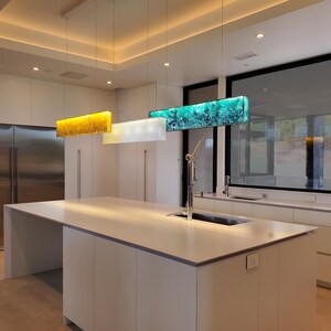 a modern kitchen with a large island, a sink, and a set of hanging pendant lights. The kitchen has a clean, minimalist design with white cabinets and stainless steel appliances.
