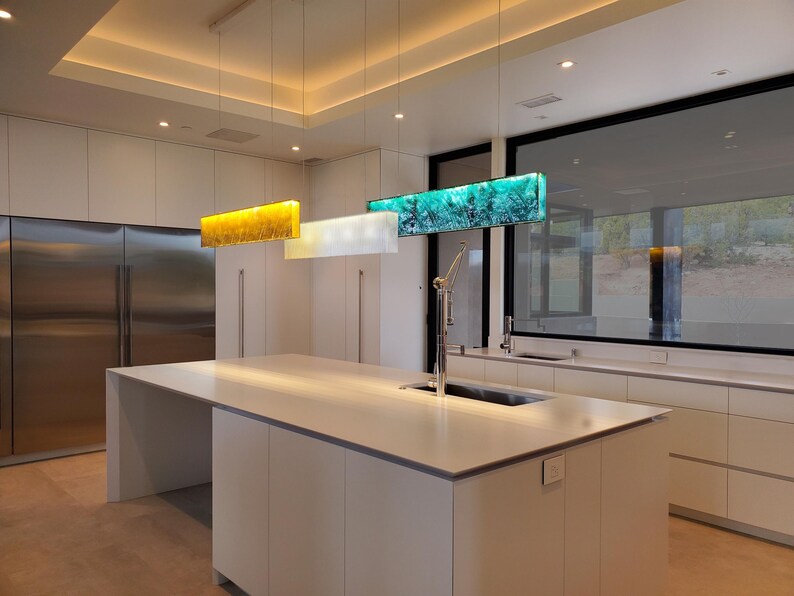 a modern kitchen with a large island, a sink, and a set of hanging pendant lights. The kitchen has a clean, minimalist design with white cabinets and stainless steel appliances.