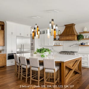 a modern kitchen with a large island, wooden cabinets, and a set of seven glass pendant lights hanging above the island.