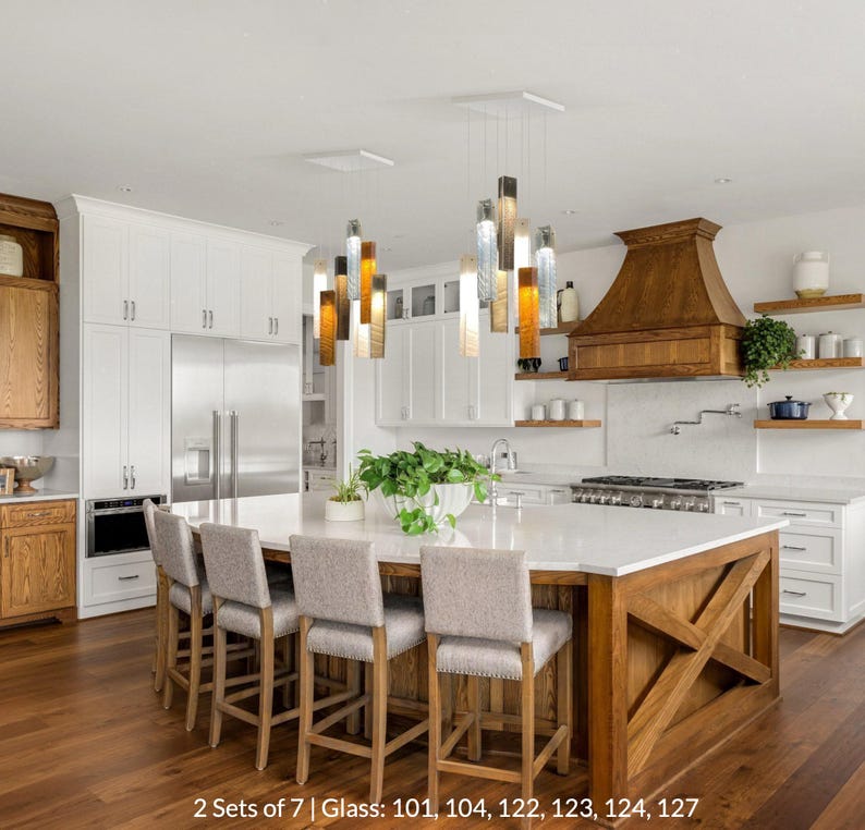 a modern kitchen with a large island, wooden cabinets, and a gas range. The kitchen is well-lit and features a large potted plant on the countertop.