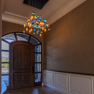a spacious entryway with a wooden door, a large arched window, and a hanging chandelier with colorful glass shades.