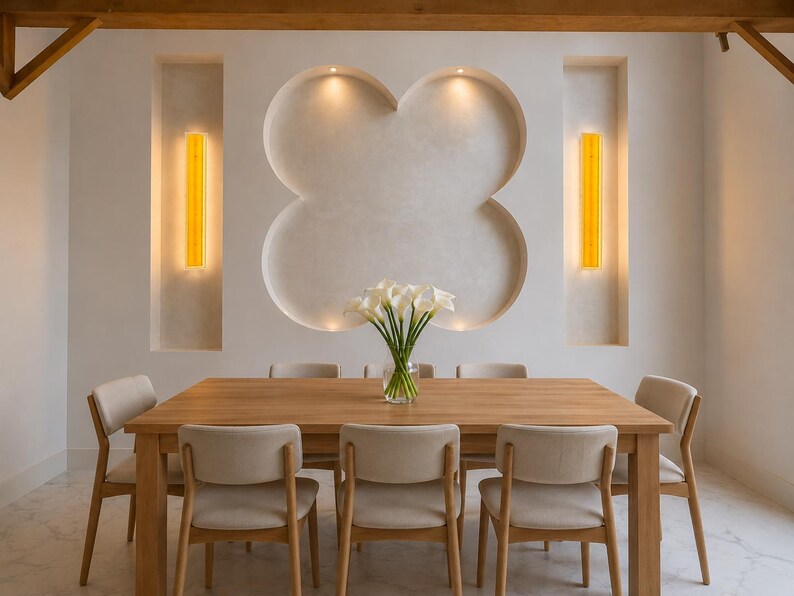 May include: A dining room with a wooden table and six beige chairs. The room features a white wall with a clover-shaped design and two vertical yellow lights. A vase of white flowers sits on the table, creating a bright and inviting space.