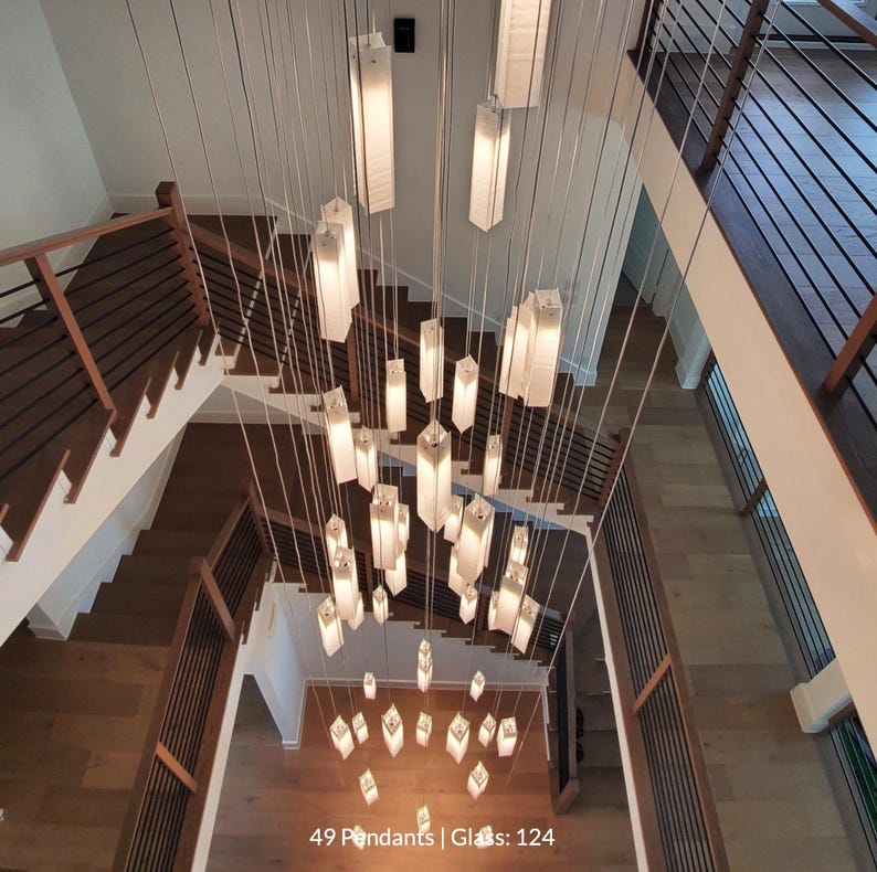 a large, intricate chandelier with numerous hanging light fixtures suspended from the ceiling. The chandelier is composed of numerous rectangular light fixtures arranged in a complex pattern, creating a visually striking and elegant display. The image is taken from a high vantage point, providing a comprehensive view of the chandelier and its surroundings.