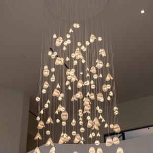 a large, intricate chandelier with numerous small, white lights suspended from the ceiling. The chandelier has a circular base and is composed of numerous hanging light fixtures, creating a visually striking and elegant display.