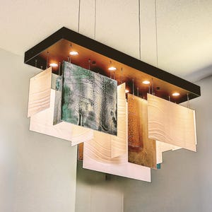 Könnte beinhalten: Eine moderne rechteckige Hängeleuchte mit einem dunkelbraunen Rahmen und mehreren hängenden Paneelen. Die Paneele sind in verschiedenen Farben gehalten, darunter Beige, Grün und Gold. Die Leuchte hat mehrere Einbaustrahler.