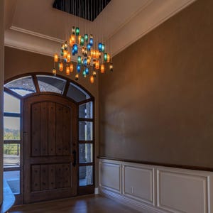 a spacious entryway with a wooden door, a large arched window, and a hanging chandelier with colorful glass shades.
