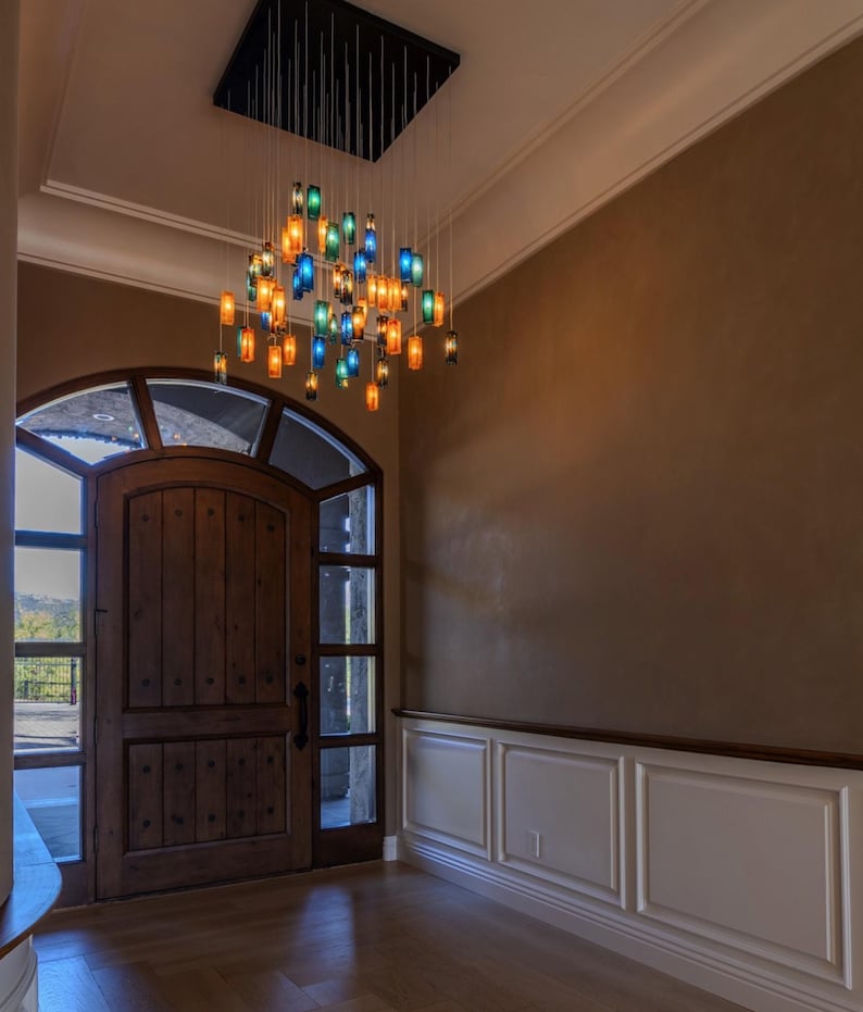 a spacious entryway with a wooden door, a large arched window, and a hanging chandelier with colorful glass shades.