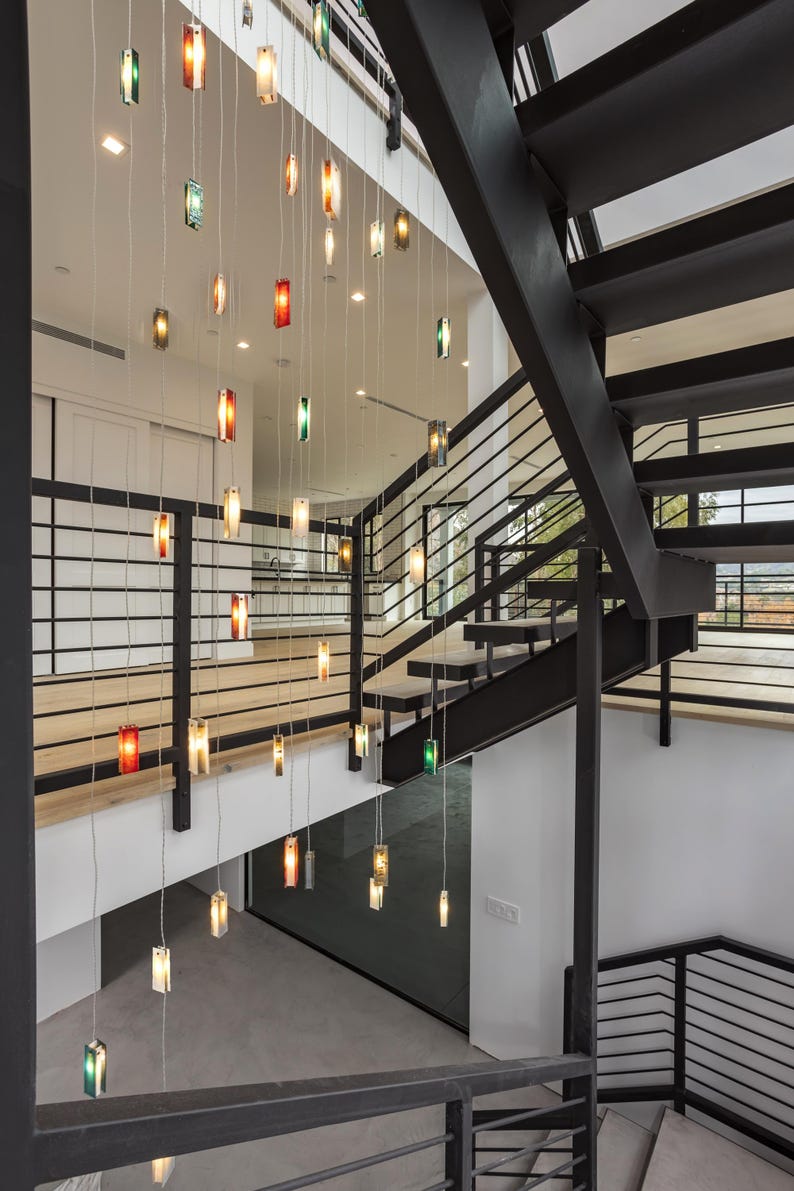 a modern interior design with a staircase and a hanging light fixture. The staircase has a black metal railing and is illuminated by a series of colorful lights suspended from the ceiling. The lights create a visually striking and contemporary atmosphere in the space.