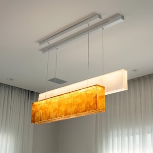 May include: A rectangular pendant light fitting suspended from a ceiling track by thin wires. The fitting consists of two stacked horizontal panels: a lower amber-coloured textured glass panel and an upper white frosted glass panel.