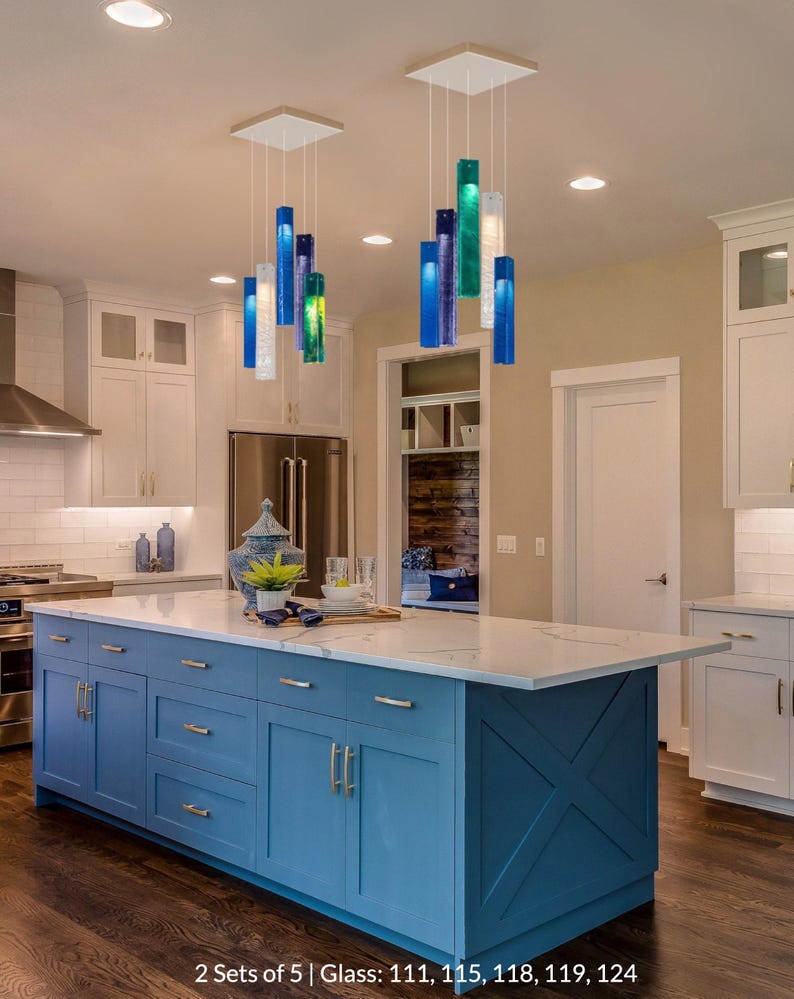 a modern kitchen with a large blue island and hanging glass pendant lights. The kitchen has white cabinets and a white tile backsplash, creating a clean and bright atmosphere.