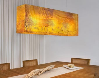 May include: A rectangular pendant light fixture with a warm amber-colored, translucent shade featuring a textured, organic pattern. The light is suspended by thin cables and emits a soft, golden glow, illuminating the space below it.