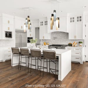 A modern, spacious kitchen with white cabinets, a large island, and a center island with bar stools. The kitchen features stainless steel appliances, pendant lighting, and a marble backsplash.