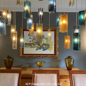 a dining room with a wooden table, three chairs, and a painting on the wall. The room has a modern and stylish design, with a mix of blue, green, and gold accents. The dining table is set with a bowl and a vase, and the chairs are arranged around the table. The painting on the wall adds an artistic touch to the space.