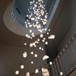 a large, intricate chandelier hanging from the ceiling of a building, composed of numerous small white lights suspended from strings.