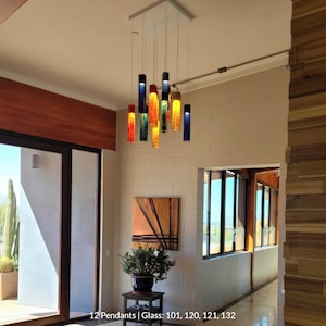 a modern interior with a hanging pendant light featuring colorful glass tubes suspended from the ceiling. The room has a wooden floor and white walls, and there is a painting on the wall. The pendant light is the focal point of the space, and the overall design appears to be contemporary and stylish.