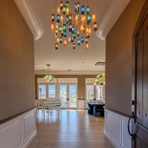 a spacious and well-lit room with a high ceiling, featuring a large chandelier with colorful glass shades hanging from the center. The room has a wooden floor and white walls, creating a warm and inviting atmosphere.