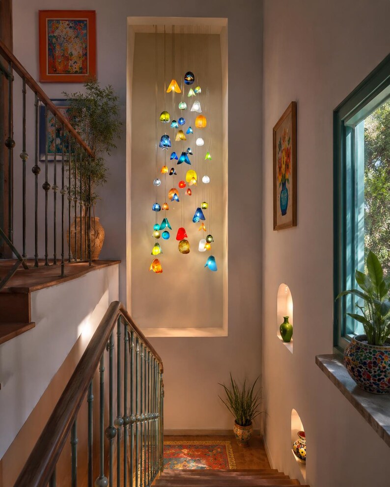 May include: A multi-colored glass pendant light installation featuring numerous small, translucent, bell-shaped and spherical glass elements in shades of blue, yellow, red, green, and white, suspended at varying heights within a recessed wall niche.