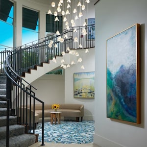A modern and stylish interior with a large staircase, a hanging chandelier, and artwork on the walls.