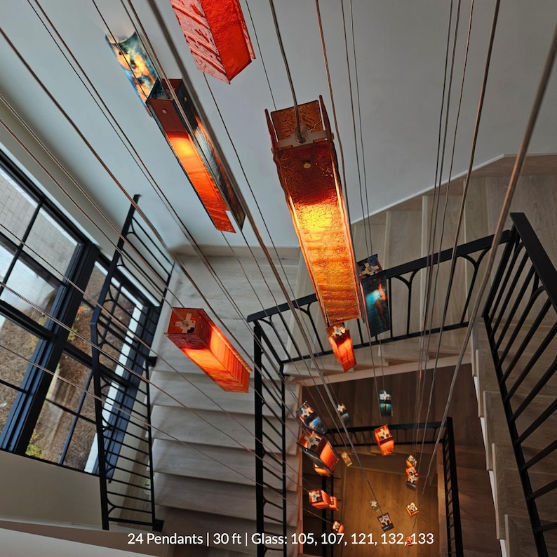 a modern interior design with a unique lighting system. The ceiling is adorned with numerous orange and red hanging lamps, creating a striking visual effect. The lamps are suspended from the ceiling by wires, adding a sense of depth and dimension to the space. The overall design is contemporary and eye-catching, with the use of vibrant colors and lighting creating a lively atmosphere.