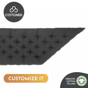 Puede incluir: Un cojín gris oscuro con mechones y forma triangular. El cojín tiene un diseño con mechones de botones y está hecho con relleno de algodón orgánico. El texto "CUSTOMIZE IT" se muestra en una barra naranja.