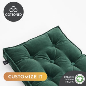 Puede incluir: Un cojín de terciopelo verde oscuro con capitoné de botones. El cojín está hecho con relleno de algodón orgánico y está certificado por GOTS. El texto "CUSTOMIZE IT" es visible en la imagen.