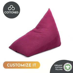 May include: A magenta beanbag chair with a triangular shape. The beanbag is made of a soft, textured fabric and features the text "CUSTOMIZE IT". The image also includes the text "COTTENED" and "ORGANIC COTTON FILLING".