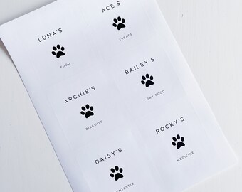 May include: Six white labels with black paw prints and text. The labels read "Ace's Treats", "Luna's Food", "Archie's Biscuits", "Bailey's Dry Food", "Daisy's Dentastix", and "Rocky's Medicine".