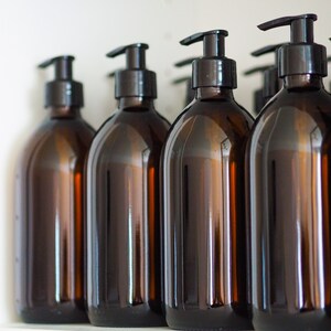 May include: Several amber-colored glass bottles with black pump dispensers are arranged in a row. The bottles have a rounded shape and are filled with a liquid. The background is a plain white surface.