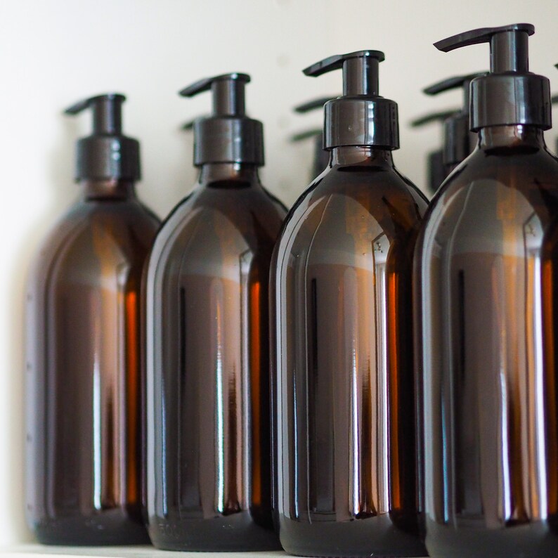 May include: Several amber-colored glass bottles with black pump dispensers are arranged in a row. The bottles have a rounded shape and are filled with a liquid. The background is a plain white surface.