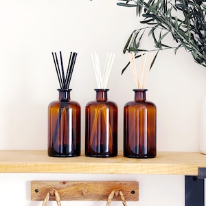 May include: Three amber glass bottles with black, white, and natural coloured diffuser sticks. The bottles are on a wooden shelf.
