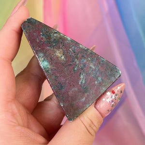 May include: A triangular-shaped polished stone with a mottled surface featuring deep burgundy, dark red, and forest green mineral inclusions. The stone has a smooth, flat face with a distinct geometric shape and varied natural color patterns.