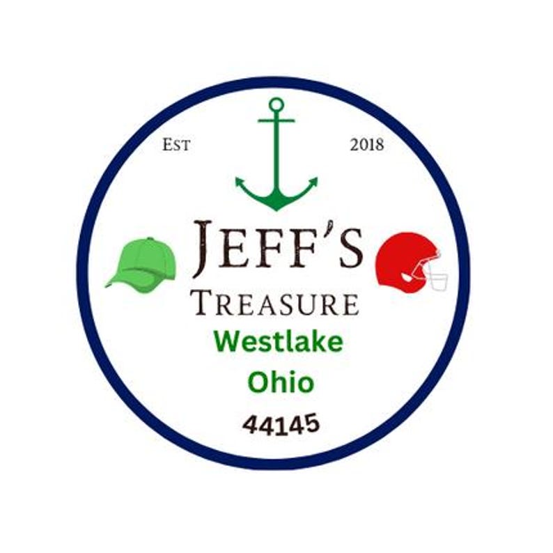 May include: A circular logo with a navy blue border. The logo features a green anchor, a green baseball cap, and a red football helmet. The text reads "JEFF'S TREASURE Westlake Ohio 44145". The logo also includes the text "EST 2018".