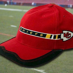 May include: A red baseball cap with a black brim and the word "CHIEFS" embroidered on the side. The cap features a white and red arrowhead logo with a "K" inside. The cap is likely a sports fan item.