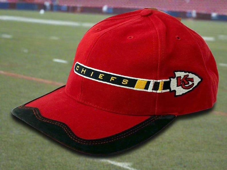 May include: A red baseball cap with a black brim and the word "CHIEFS" embroidered on the side. The cap features a white and red arrowhead logo with a "K" inside. The cap is likely a sports fan item.
