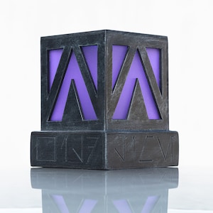 May include: A black cube with a purple geometric pattern inside. The cube is sitting on a black base with the text "IN7" and "J1EV" on the front and back.