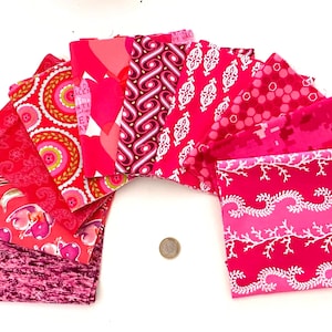 Peut inclure: Une collection de carrés de tissu dans diverses nuances de rose et de magenta, disposés en éventail. Les motifs incluent des cœurs, des fleurs, des formes géométriques et des designs abstraits. Une petite pièce circulaire est placée au centre.