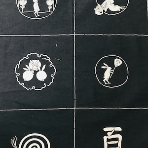 Op de afbeelding: Een zwarte stof met witte borduursels die een reeks Japanse zomermotieven voorstellen. De motieven omvatten een konijn dat een waaier vasthoudt, een konijn onder een maan met sterren, een konijn dat een perzik vasthoudt, een konijn met een spiraal en het kanji-teken voor zomer.