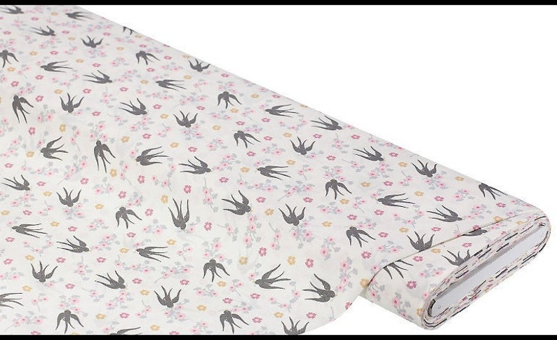 May include: White fabric with a repeating pattern of small pink flowers and black silhouettes of birds. The fabric is rolled up and the end is visible.