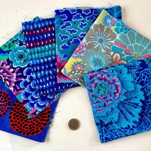 Op de afbeelding: Een verzameling van zes vierkante stoffen lappen met levendige bloemen- en geometrische patronen in tinten blauw, paars, roze en geel, waaiervormig gerangschikt naast een kleine ronde munt voor schaalvergelijking.