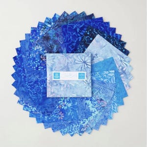 Puede incluir: Una pila de piezas de tela cuadradas dispuestas en un patrón de abanico circular. La tela presenta varios tonos de azul con patrones florales y abstractos. Una banda de papel blanco envuelve el centro con el texto Island Batik 42 Charms 5 Squares.
