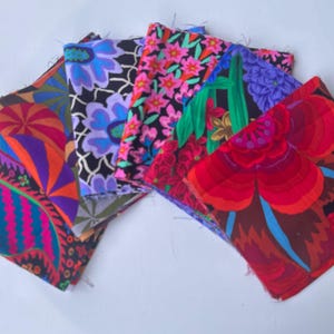 Könnte beinhalten: Eine Sammlung farbenfroher Stoffquadrate mit floralen Mustern. Die Stoffe weisen eine Vielzahl von Designs auf, darunter große rote Blumen, blaue und violette Blüten und abstrakte Formen in Orange, Rosa und Grün. Die Quadrate sind fächerförmig angeordnet.