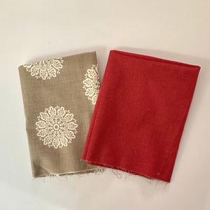 Peut inclure: Deux morceaux de tissu pliés. L'un est de couleur beige avec un motif floral blanc. L'autre est de couleur rouge uni. Les deux pièces ont un bord brut. Les tissus sont probablement destinés à la couture ou à l'artisanat.