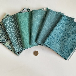 Può includere: Un set di sei quadrati di tessuto in varie tonalità di verde con diversi motivi. I quadrati di tessuto sono disposti a forma di ventaglio.