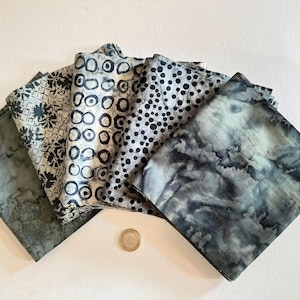 Puede incluir: Una colección de cuatro cuadrados de tela doblados con patrones en blanco y negro que incluyen una cuadrícula floral, círculos concéntricos, puntos pequeños y un diseño de lavado marmoleado, dispuestos en abanico junto a una pequeña moneda metálica.