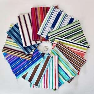 Peut inclure: Un ensemble d'échantillons de tissu colorés disposés en cercle. Chaque échantillon présente un motif à rayures unique, avec des couleurs variées comme le bleu, le vert, le rouge et le marron. Un bouton argenté est au centre.