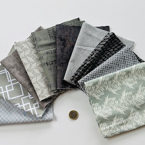 Puede incluir: Una colección de muestras de tela en varios tonos de gris y verde con patrones geométricos y abstractos. Las muestras están dispuestas en semicírculo sobre una superficie blanca.