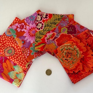 Peut inclure: Plusieurs carrés de tissu pliés avec des motifs floraux audacieux en rouge, orange, rose et violet. Les motifs comprennent de grandes fleurs et des motifs plus petits et pointillés. Une petite pièce de monnaie est également visible.