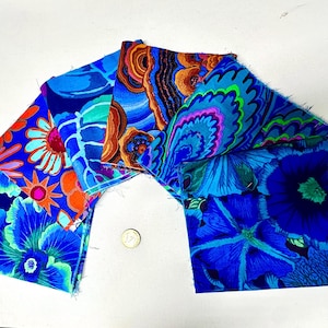 Puede incluir: Una colección de seis muestras de tela cuadradas dispuestas en abanico, con vibrantes patrones florales y abstractos en tonos azul, morado, naranja y verde. Una pequeña moneda de color dorado está colocada en el centro como referencia de escala.