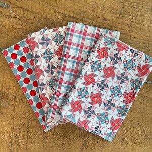 Peut inclure: Quatre carrés de tissu aux motifs patriotiques. Les motifs comprennent des pois rouges, des moulins à vent avec des étoiles et des rayures, du tartan rouge et bleu, et des moulins à vent avec des étoiles et des rayures rouges, blanches et bleues.